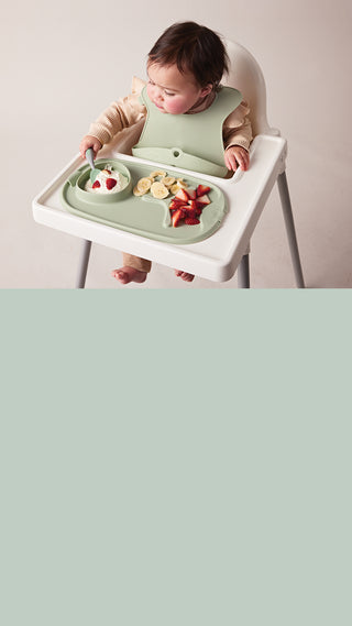 baby girl sitting at high chair eating from roll + go mealtime mat